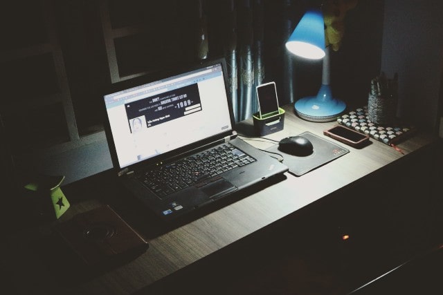a desk with a laptop, desk lamp, mouse, and cell phone